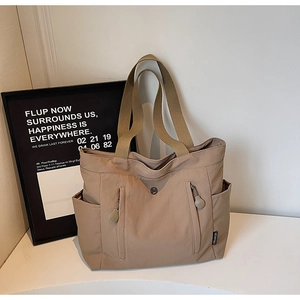 Detail of khaki canvas tote bag featuring dual front zippers and side utility pockets