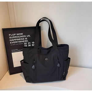 Detail of black nylon tote bag featuring front dual zippers and wide shoulder straps