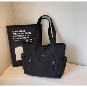 Detail view of the black canvas tote bag showing side zipper pockets and durable fabric