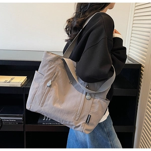 Detail view of grey nylon tote bag with side pocket and metal M-embossed zipper