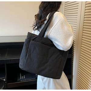 Detailed back view of a large black quilted nylon tote bag worn by a model in a modern room