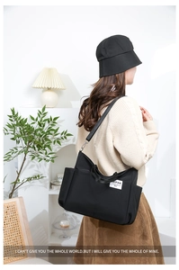 Detail of a black nylon shoulder bag showing the side pocket and logo on model