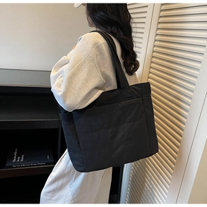 Quilted black tote bag shown on model featuring a puffy texture and spacious side pocket