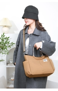 Detail of khaki nylon tote bag showing side pockets and adjustable shoulder strap worn by model