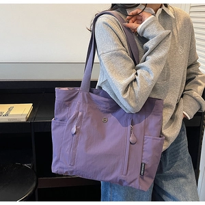 Detail of purple waterproof nylon tote bag showing zipper pockets and woven shoulder strap