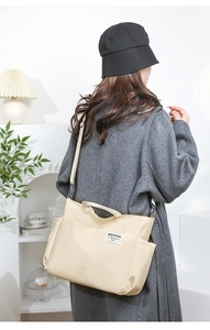 Model wearing a cream nylon tote bag with adjustable shoulder strap in a minimalist setting