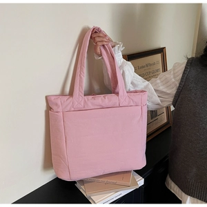 Pink quilted tote bag shown with a wide shoulder strap in a stylish home setting