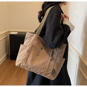 Detail of khaki tote bag showing side pockets and woven brand tag on high-quality fabric
