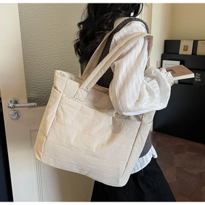 Detail of cream quilted tote bag with side pockets and wide strap in cozy indoor setting