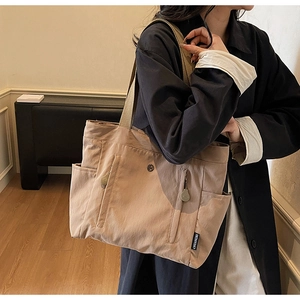 Detail of khaki nylon tote bag showing side pockets and black brand logo label