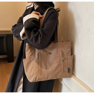 Detailed close-up of khaki nylon tote bag showing front zipper pockets and fabric texture