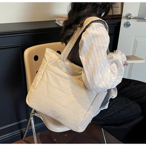 Detailed side view of a large cream-white fabric tote bag worn by a model in a minimal setting