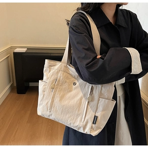Close-up of minimalist off-white nylon tote bag with functional pockets and woven label