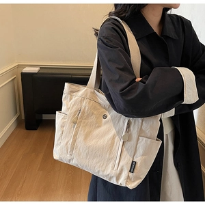 Detail of cream nylon tote bag with double front zippers and side pockets on a model