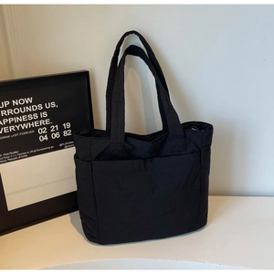 Detail of black quilted nylon tote bag with side pockets on a minimalist white stage