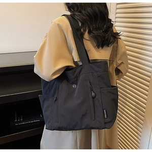 Side view of black nylon shoulder bag with wide strap and zip pocket detail