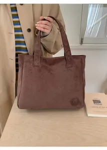 Detail of a brown suede tote bag with round embossed logo and minimalist stitching