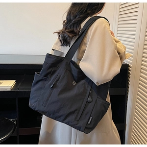 Detail of black nylon tote bag featuring front zipper pockets and woven shoulder strap