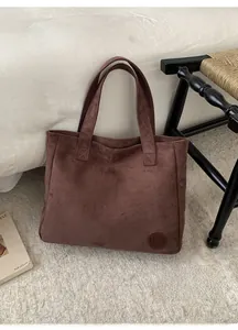 Detail of soft dark brown suede tote bag with circular embossed logo in cozy room