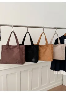 Detail view of large corduroy tote bags in brown, black, and beige colors on hangers