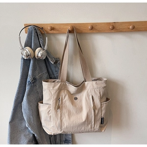 Detail of beige nylon tote bag with functional exterior zipper pockets and wide shoulder strap