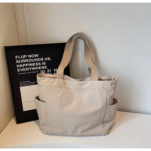 Close-up of beige nylon tote bag showing wide handles and functional side pockets