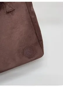 Detail of dark brown tote bag showing fine suede texture and circular leather logo patch