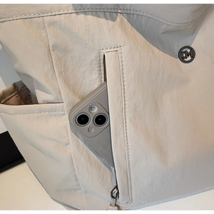 Detail showing the side zipper pocket of a beige nylon bag containing a smartphone