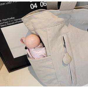 Detail of beige nylon tote bag side pocket with pink umbrella and branded zipper pull