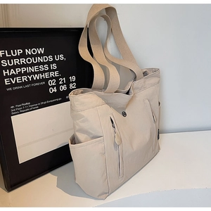 Detail view of beige nylon tote bag with side pocket and reinforced fabric strap