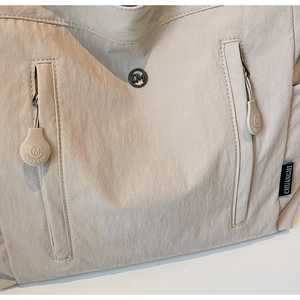 Detail view of beige nylon bag showing metal CM logo and zipper pocket with brand tag