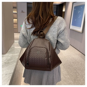 Rear view of a dark brown woven leather backpack worn on shoulder in a minimalist setting