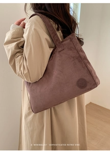 Close-up of a large brown suede tote bag with a circular logo on a minimalist trench coat