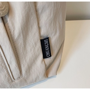 Detail of minimalist nylon bag showing woven label, snap button, and textured fabric surface
