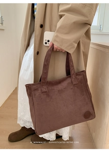 Detail of a brown suede tote bag with embossed logo and wide shoulder straps on a model