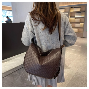 Detail of dark brown woven leather tote bag with wide strap on shoulder