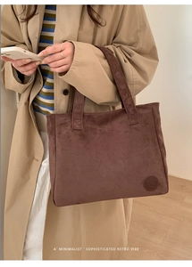 Detail of a brown suede tote bag featuring a round embossed logo and textured surface