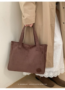 Detail of dark brown matte tote bag held by model wearing a trench coat and retro boots