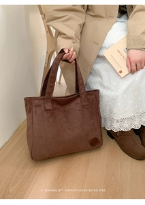 Detail of dark brown suede tote bag featuring a round embossed logo and wide straps