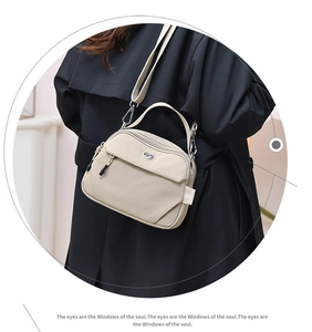 Détail d'un sac bandoulière en nylon beige avec zip métallique sur un manteau noir