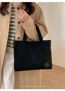 Detail of black textured corduroy tote bag featuring a round embossed brand patch logo