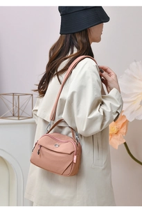 Mannequin portant un sac à bandoulière en nylon rose pêche avec plusieurs fermetures