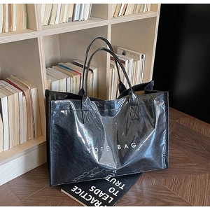 Detailed view of a black glossy tote bag with white TOTE BAG text on a wooden shelf