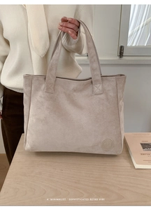 Detail of minimalist beige suede tote bag featuring debossed logo and durable handle