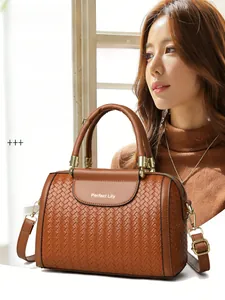 Close-up of brown woven texture Boston bag with elegant golden hardware and top handles