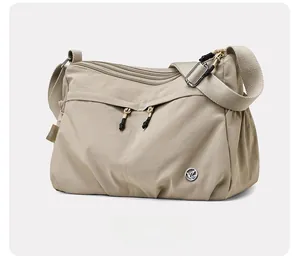 Detail view of water-resistant beige nylon crossbody bag with adjustable strap and metal logo