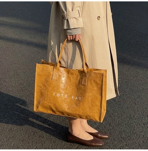 Close-up of brown textured Tyvek tote bag with white TOTE BAG print in outdoor sunlight