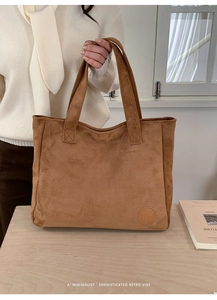 Close-up of camel suede tote bag showing embossed logo detail and reinforced stitching