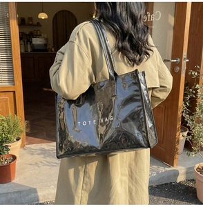 Fashionable black high-gloss tote bag shown on shoulder in a warm cafe setting