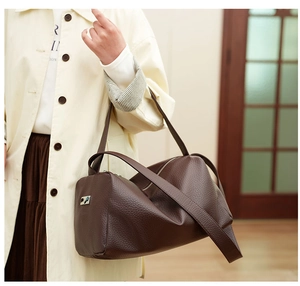 Detail of dark brown pebble leather cylinder bag with wide strap and silver metal logo